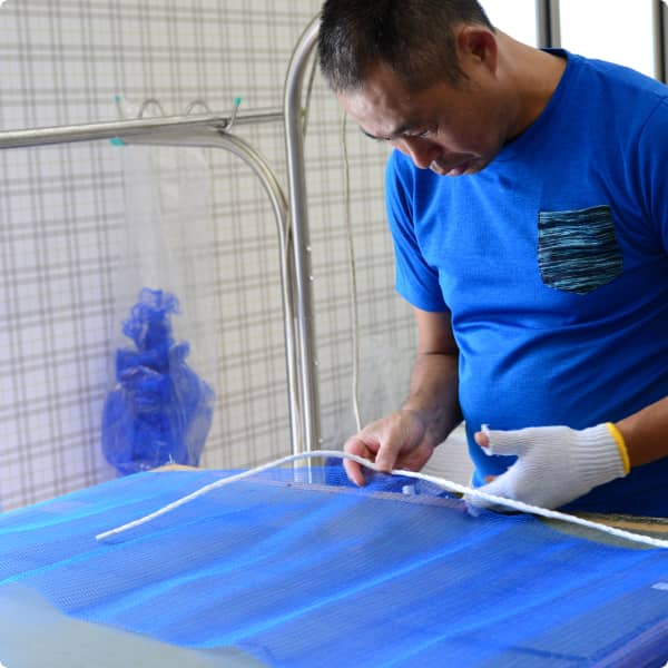 青いネットに白い紐を縫い付けている男性