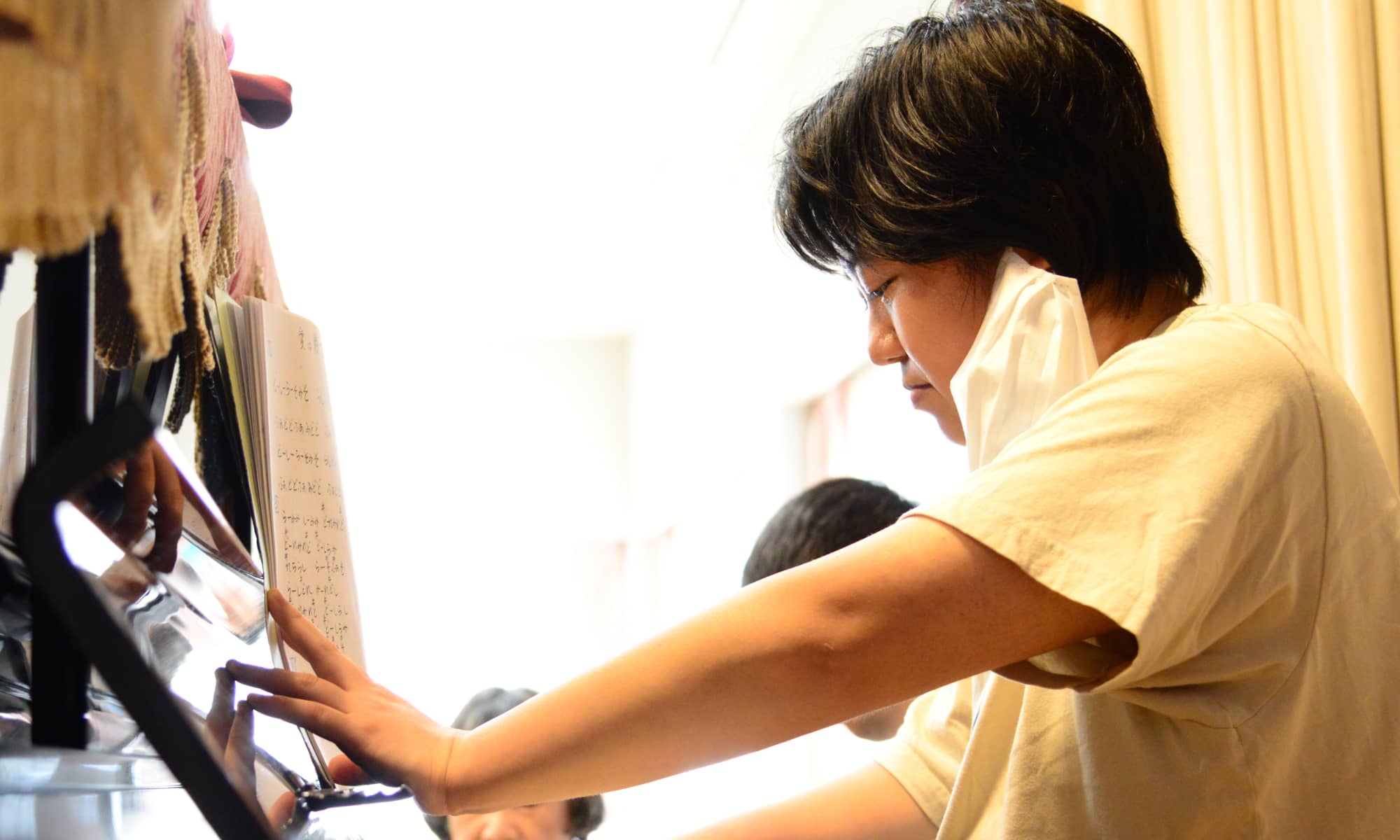 ピアノに向かい楽譜を確認しながら演奏する女性。集中した表情が印象的