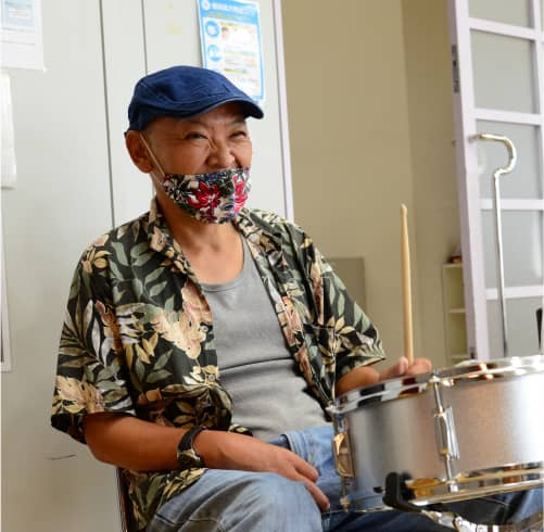 帽子と柄シャツを着た男性がドラムを叩こうとしている様子