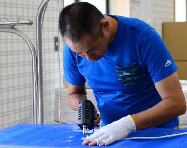青い布を加工する男性の作業風景
